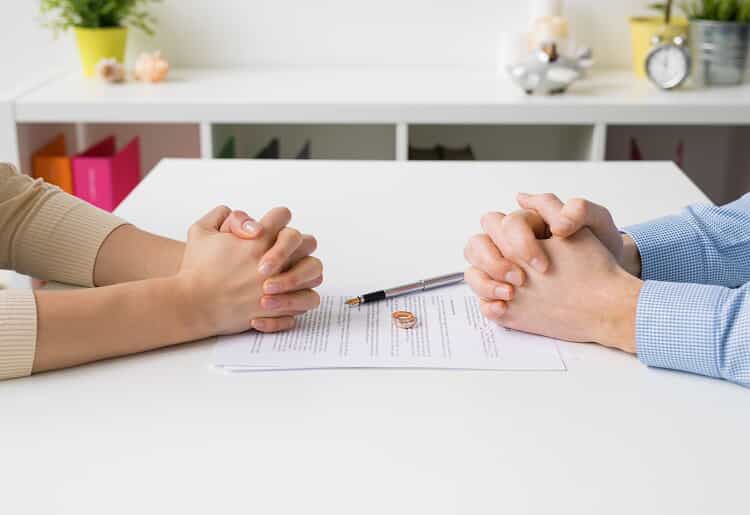 Couple sitting in front of each other with hands clasped. Their rings and Las Vegas divorce paperwork is on the table.